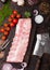 Fresh raw pork ribs on chopping board and vintage meat hatchets on wooden background. Fresh tomatoes and red onion with garlic