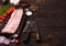 Fresh raw pork ribs on chopping board and vintage meat hatchets on wooden background. Fresh tomatoes and red onion with garlic