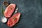 Fresh raw Prime Black Angus beef steaks on stone board: Striploin, Rib Eye. Top view with copy space. On a dark background