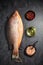 Fresh raw red snapper fish with red pepper, olive oil and Himalayan rock salt on dark background. Top view. Vertical composition