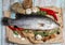 Fresh Raw Sea Bass on wooden table surrounded by fresh ingredients and spices