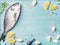 Fresh raw sea bream fish decorated with lemon slices, spices and shells on blue wooden background, copy space
