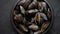 Fresh and raw sea mussels in black ceramic bowl placed on dark stone background