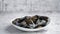 Fresh and raw sea mussels in white ceramic bowl on stone background