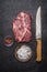 Fresh raw steak with red pepper and salt with carving knife on a dark rustic background top view