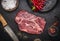 Fresh raw steak with red pepper salt pan carving knife on a dark rustic background top view close up