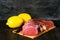 Fresh raw veal tenderloin in a large piece with lemons, sprig of rosemary and garlic on a dark vintage background.