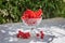 Fresh red currant in a crystal glass stand on a table with a white cloth on the background of blurred flowers. Fresh harvest.