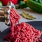 Fresh red meat mincing with old metal manual grinder, viewed in close-up on grey stone background .