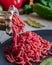 Fresh red meat mincing with old metal manual grinder, viewed in close-up on grey stone background .