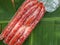 Fresh red pork Chinese sausage stuffed in a vacuum plastic bag placed on a fresh green banana leaf. It is a popular dried food tha
