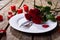 Fresh red roses with cutlery on plate by petals and burning candles at wooden table