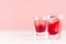Fresh red strawberry cocktails with ice cubes in two elegant misted shot glasses on soft light pink color background.