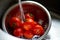 Fresh red tomatoes splashing in water before cooking at home, washes in a metal sink in the kitchen