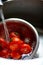 Fresh red tomatoes splashing in water before cooking at home, washes in a metal sink in the kitchen