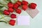 Fresh red tulips and white sheet of paper with mail envelope on light green background. Top view. Copy space