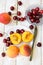 Fresh ripe colorful halved and whole peaches on white plate, scattered sweet cherries on plank wood table