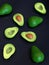 Fresh ripe green avocado fruits, whole and cut in half, on black