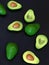 Fresh ripe green avocado fruits, whole and cut in half, on black