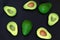 Fresh ripe green avocado fruits, whole and cut in half, on black