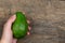 Fresh ripe organic green avocado in female hands on woden table, top view summer food concept