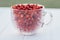 Fresh ripe peeled small wild strawberries in big transparent glass round mug on light blue background. close up.
