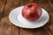 A fresh ripe pomegranate lies on a white saucer on a brown Board.