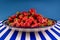 Fresh ripe red strawberries on a huge earthenware dish on a blue-and-white striped table.