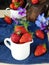 Fresh ripe strawberries in a ceramic jug surrounded by pansies and berries