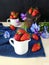 Fresh ripe strawberries in a ceramic jug surrounded by pansies and berries