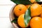 Fresh ripe tangerines with leaves in wooden bowl on table, closeup. Citrus fruit