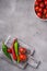 Fresh ripe tomatoes in bowl near to old wooden cutting board with hot chili peppers, stone concrete background