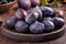 Fresh ripe whole purple damson plums on wooden plate