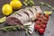 Fresh river fish on a metal tray. Lemon and sprig of cherry tomato and rosemary