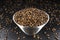 Fresh, roasted coffee beans in a glass bowl, standing on a black table, with lots of coffee scattered around.