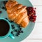Fresh ruddy croissants with berries lie on a wooden table next to fresh black currant berries, red currants