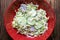 Fresh salad of autumn vegetables - green cabbage, cucumber, purple onions, parsley - in a red bowl on rustic wooden table. Rich