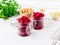 Fresh salad of grated boiled beetroot in jars, white wooden background, side view.