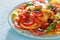 Fresh salad with red and yellow tomato slices, basil, olives and spices on blue plate.