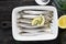 Fresh sea cold-water small fish such as smelt, sardine, anchovies on a simple background with lemon slices, for the