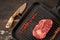 Fresh, seasoned ribeye steak in a grill pan with sprinkled spices, dried tomatoes and paprika, a hunting knife and a kitchen knife