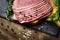 fresh sliced beef pastrami surrounded by herbs in wooden chopping board