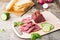 Fresh sliced marbled beef pastrami, cucumber, radish and basil on a cutting board. American delicacy. Rustic style