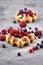 Fresh small round waffles topped with fruits like blueberry and cranberry and powdered sugar