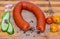 A fresh smoked sausage horseshoe shape with bacon and sliced green cucumber and three red and yellow tomatoes cherry and