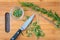 Fresh sprigs of rosemary with on a bamboo cutting board, paring knife, rosemary leaves, chopped rosemary in small glass bowl