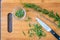 Fresh sprigs of rosemary with on a bamboo cutting board, paring knife, rosemary leaves, chopped rosemary in small glass bowl