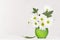 Fresh spring chamomile bouquet with leaf in bright green glass vase on white wood table and soft light background.