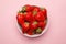 Fresh strawberries in a bowl on pink background