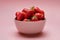 Fresh strawberries in a bowl on pink background